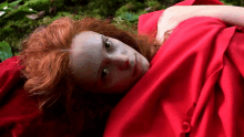 a woman with red hair laying on a red blanket