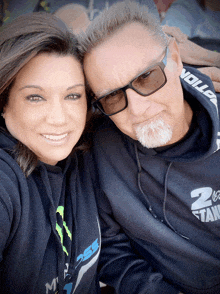 a man and a woman are posing for a picture with the man wearing a hoodie that says 2 on it