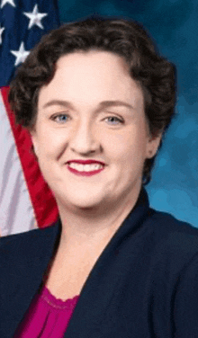 a woman stands in front of an american flag and smiles for the camera