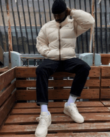 a man wearing a fila jacket sits on a wooden pallet