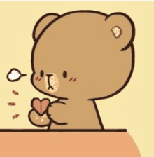 a brown teddy bear is sitting at a table holding a heart in its paws .