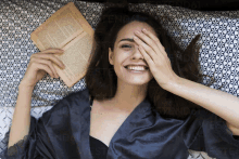 a woman laying on a bed covering her eyes with her hand while reading a book