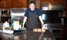 a man in an apron stands in a kitchen next to a bowl of eggs and a gallon of milk