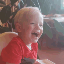 a young boy wearing a red shirt is laughing with his mouth open