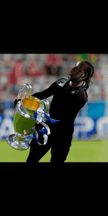 a man in a black shirt is holding a trophy on a field