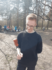 a man in a black sweater holds a sausage on a stick