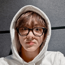 a young man wearing a white hoodie and glasses .