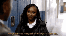 a woman in a leather jacket is talking to a man in a hallway while standing next to lockers .