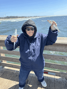 a woman in a blue jacket is holding a small fish on a pier