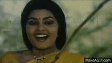 a woman in a yellow sari is smiling with a stick in her mouth .