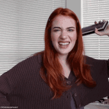 a woman with red hair is smiling and holding a book in front of a window with blinds and the words itsthewalshfamily below her