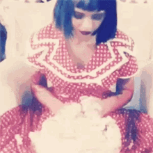 a woman in a red and white polka dot dress is sitting in a chair with a cake in front of her .