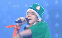 a man is singing into a microphone while wearing a green shirt and hat .