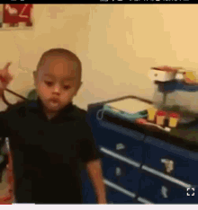 a young boy in a black shirt is standing in front of a blue dresser holding a rope around his neck