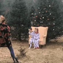 a woman is taking a picture of two little girls sitting in a chair in front of a christmas tree