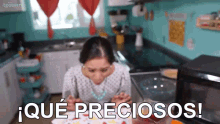 a woman is sitting in a kitchen with a plate of food and the words que preciosos in front of her