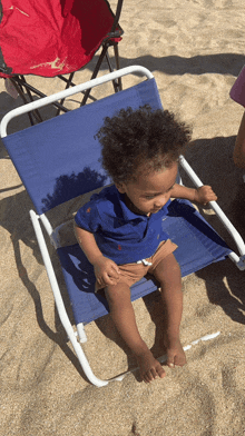 a toddler sits in a blue chair on the beach