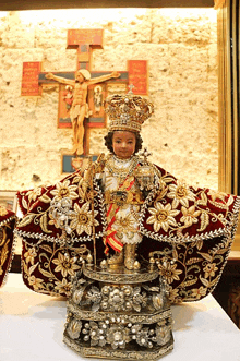 a statue of jesus wearing a crown and a robe with a cross in the background