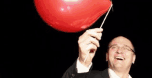 a man in a suit is holding a red balloon with a needle in it .