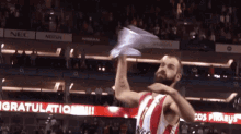 a man in a red and white jersey holds up a paper airplane in front of a sign that says " congratulations "