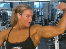 a woman is flexing her muscles in a gym wearing a black tank top with the word muscles on it