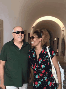 a man wearing sunglasses and a woman wearing a floral dress smile for the camera