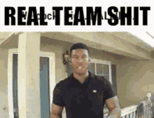 a man in a black shirt is standing in front of a house and says real team shit .