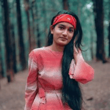 a woman in a red dress and a red bandana is standing in the woods .