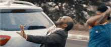 a man in a suit is standing next to a car with a bottle of beer on his neck .