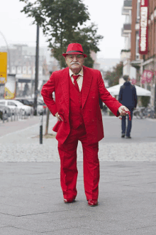 a man in a red suit and hat stands on a sidewalk in front of a restaurant