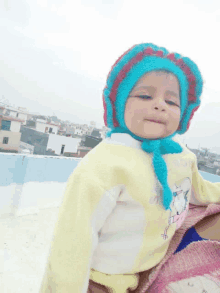 a baby wearing a blue and red hat and a yellow sweater with a cat on it