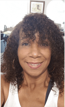 a woman with curly hair wearing a white tank top smiles for the camera