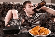 a man drinking a beer while holding a remote control and a bowl of chips