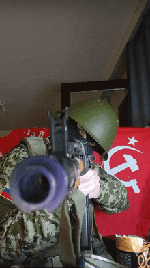 a man holding a gun in front of a red flag with the hammer and sickle on it