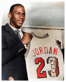 a man in a suit and tie is holding up a jersey that says jordan 23