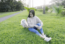 a woman is sitting in the grass with a small white dog