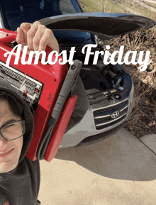 a man is holding a red jump starter in front of a car with the word almost friday on the bottom