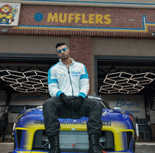 a man sits on the front of a race car in front of a building that says mufflers