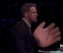 a man in a suit and tie holds up a giant hand