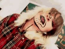 a woman in a plaid shirt has a drawing of a cat on her face .