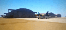 a yellow and black fighter jet is parked in front of a hangar