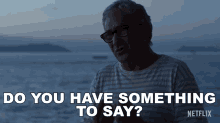 a man with glasses says " do you have something to say " in front of the ocean