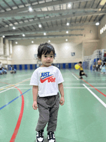 a little boy wearing a just do it shirt stands on a gym floor