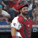 a baseball player wearing a helmet and catcher 's gear stands in front of a banner that says bally sports