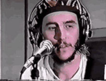 a man with a beard is wearing headphones and a hat and singing into a microphone .