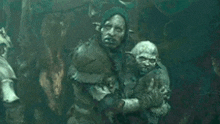 a man is holding a small orc in his arms in a cave .