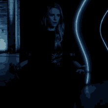 a woman in a black dress is standing in a dark room with a neon light behind her