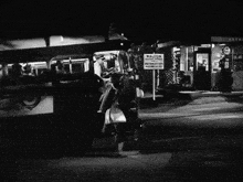 a black and white photo of a man holding a briefcase in front of a bus that says ' king '