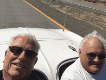 two men wearing sunglasses are sitting in the back of a white car