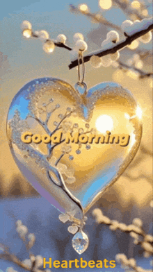 a heart with the words good morning written on it is hanging from a tree branch